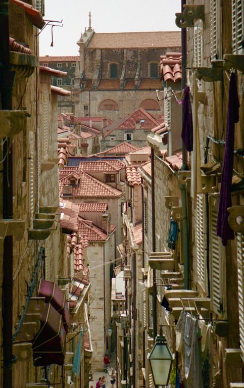 A narrow street in Dubrovnik is lined with buildings with red tile roofs and laundry hanging from windows.