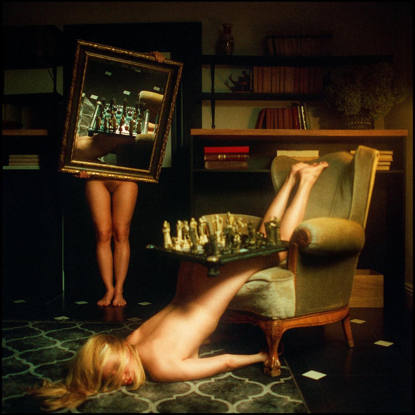 A nude woman lies on the floor with a chessboard on her leg while another nude woman holds a mirror reflecting a chessboard.