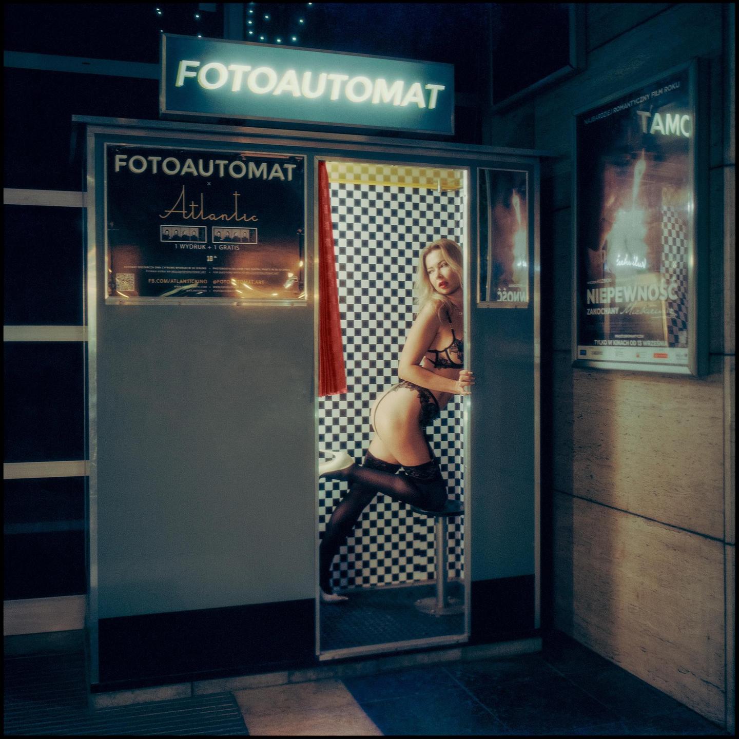 A woman in lingerie poses in a photo booth with a checkered background.