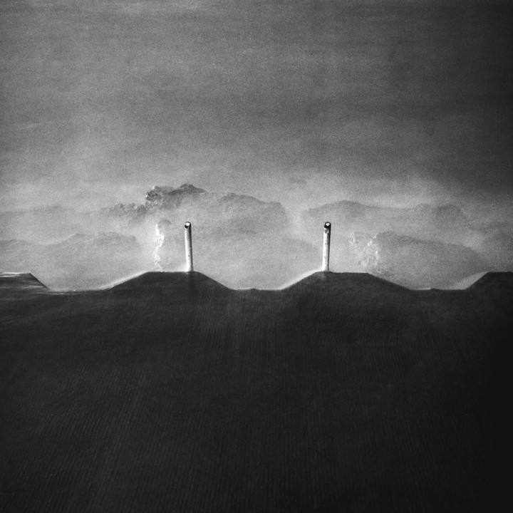 Two white pipes emerge from dark, undulating ground with a hazy, mountainous background.