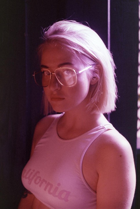 A woman with blonde hair and glasses wears a pink top with "California" written on it.