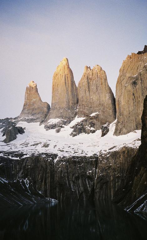 Snow-covered mountains rise above a body of water, with the peaks illuminated by golden light.