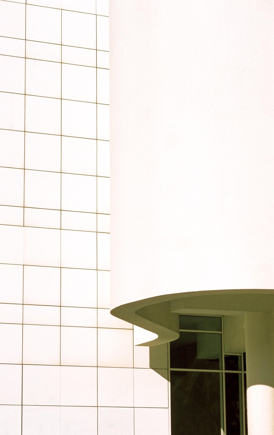 A white building with a grid pattern on one side and a curved, wavy architectural feature on the other.