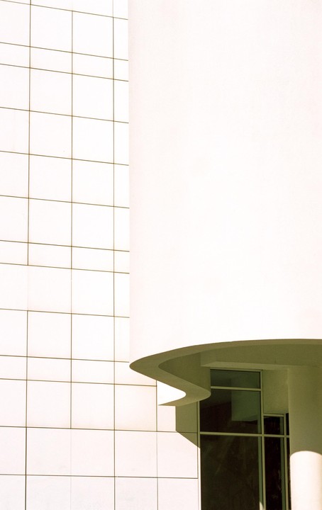 A white building with a grid pattern on one side and a curved, wavy architectural feature on the other.