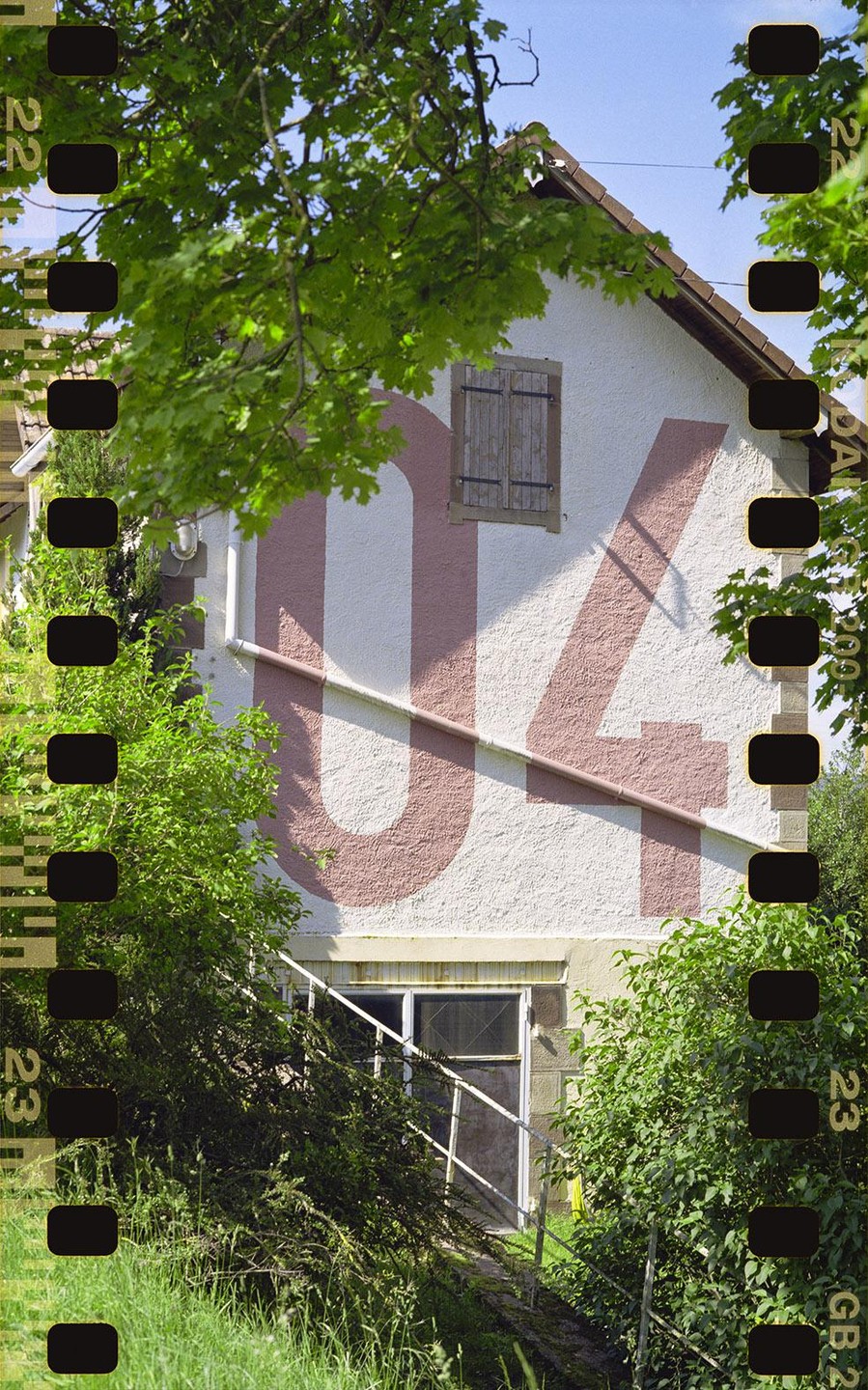 A large number 04 is painted on the side of a white house with a single window and shutter.
