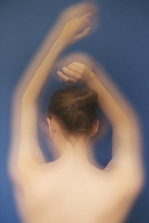 A woman with her back to the viewer raises her arms against a blue background.