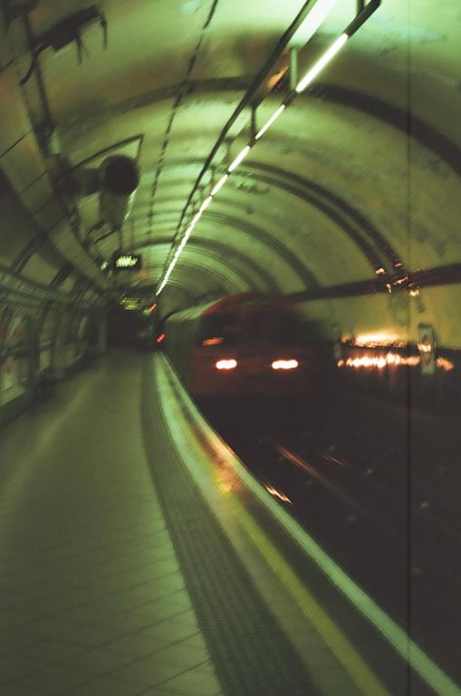 A subway train with bright headlights approaches a platform in a dark, arched tunnel.