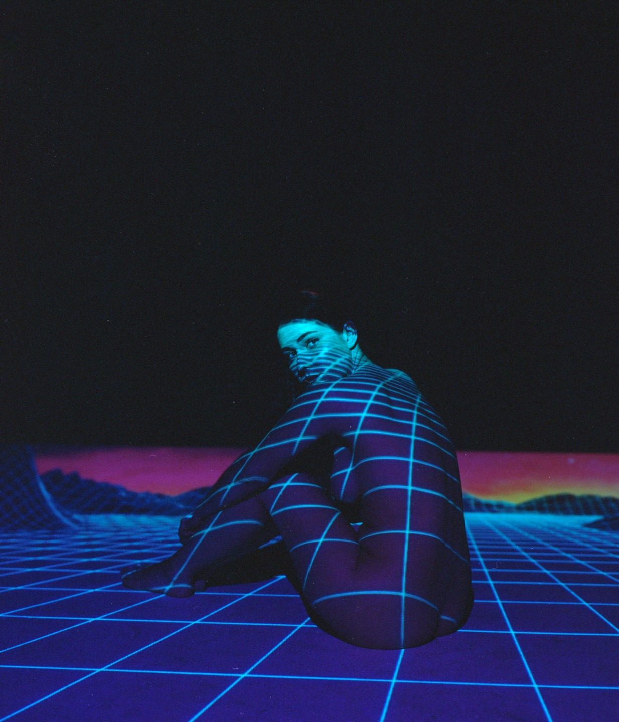 A woman sits on a grid-patterned surface with a grid projected onto her body and a purple and blue landscape in the background.