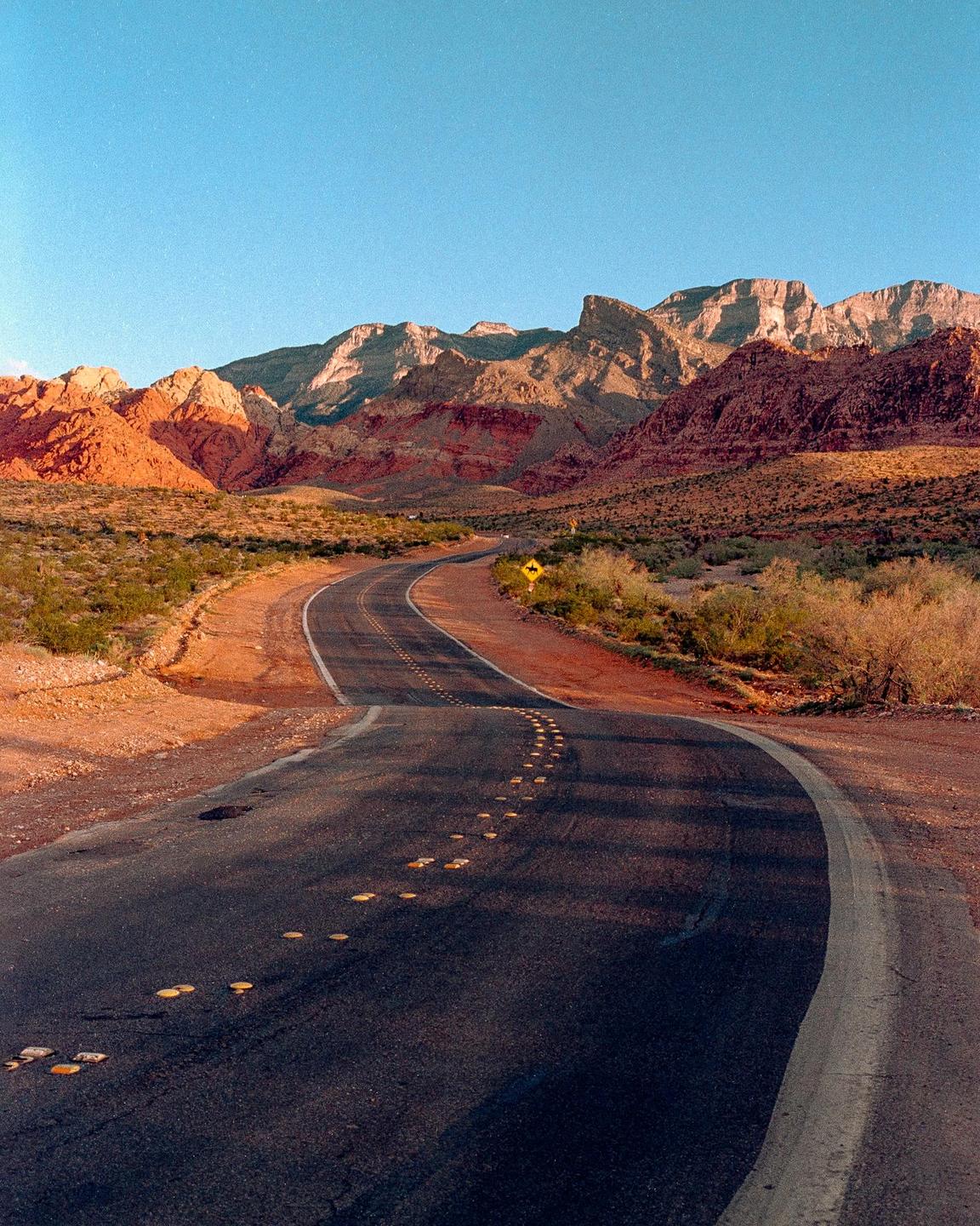 A winding road leads through a desert landscape with mountains in the background.