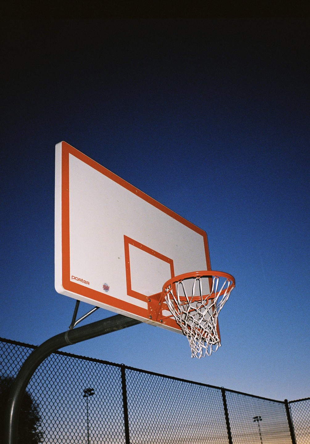 A basketball hoop and backboard are visible against a gradient blue sky at dusk.
