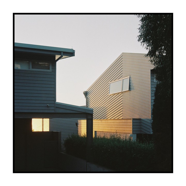 The sun illuminates the side of a modern building with horizontal siding and a small window.