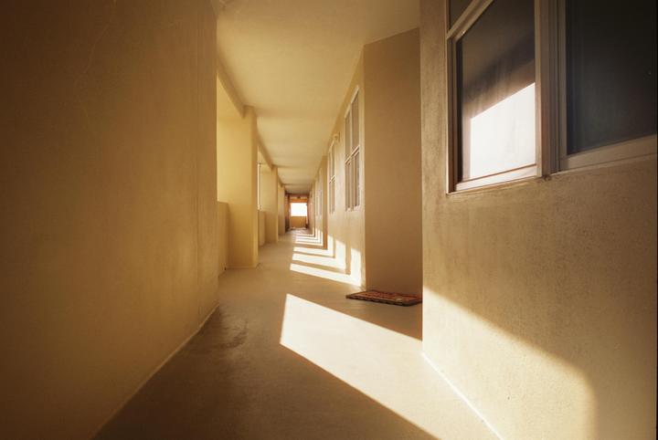Sunlight streams through windows, casting shadows across a long, empty hallway.