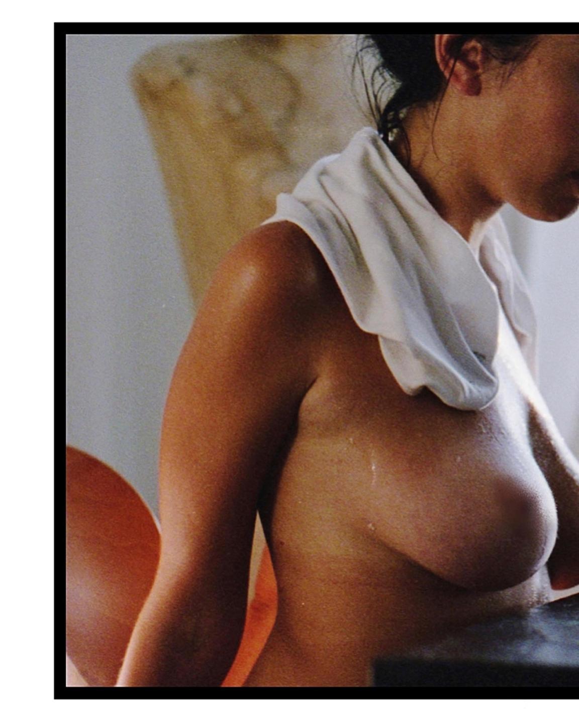 A woman with a white cloth around her neck is seen from the chest up, with drops of perspiration on her skin.