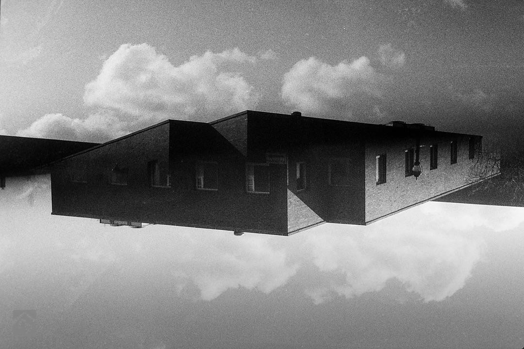 A brick building with many windows appears to float upside down in a cloudy sky.