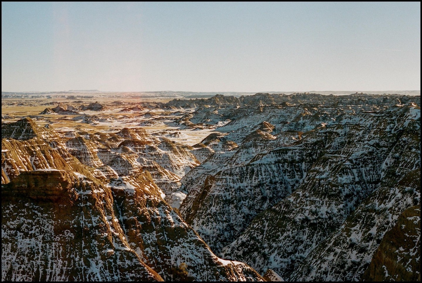 A vast landscape of snow-dusted badlands stretches under a clear sky.