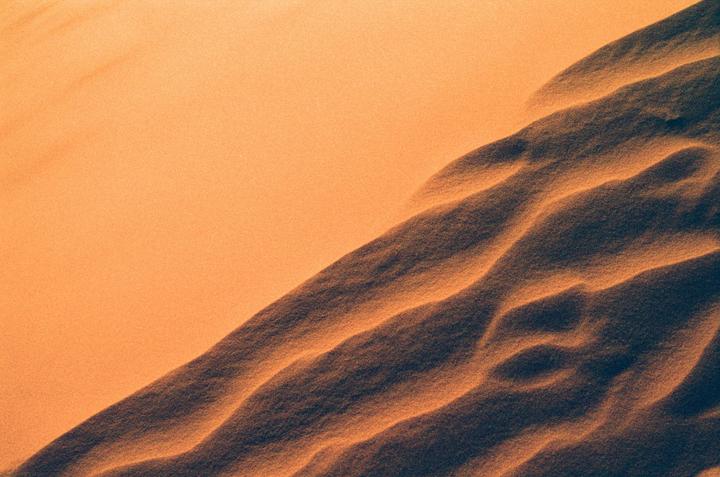 A close-up view of sand dunes shows patterns of light and shadow.