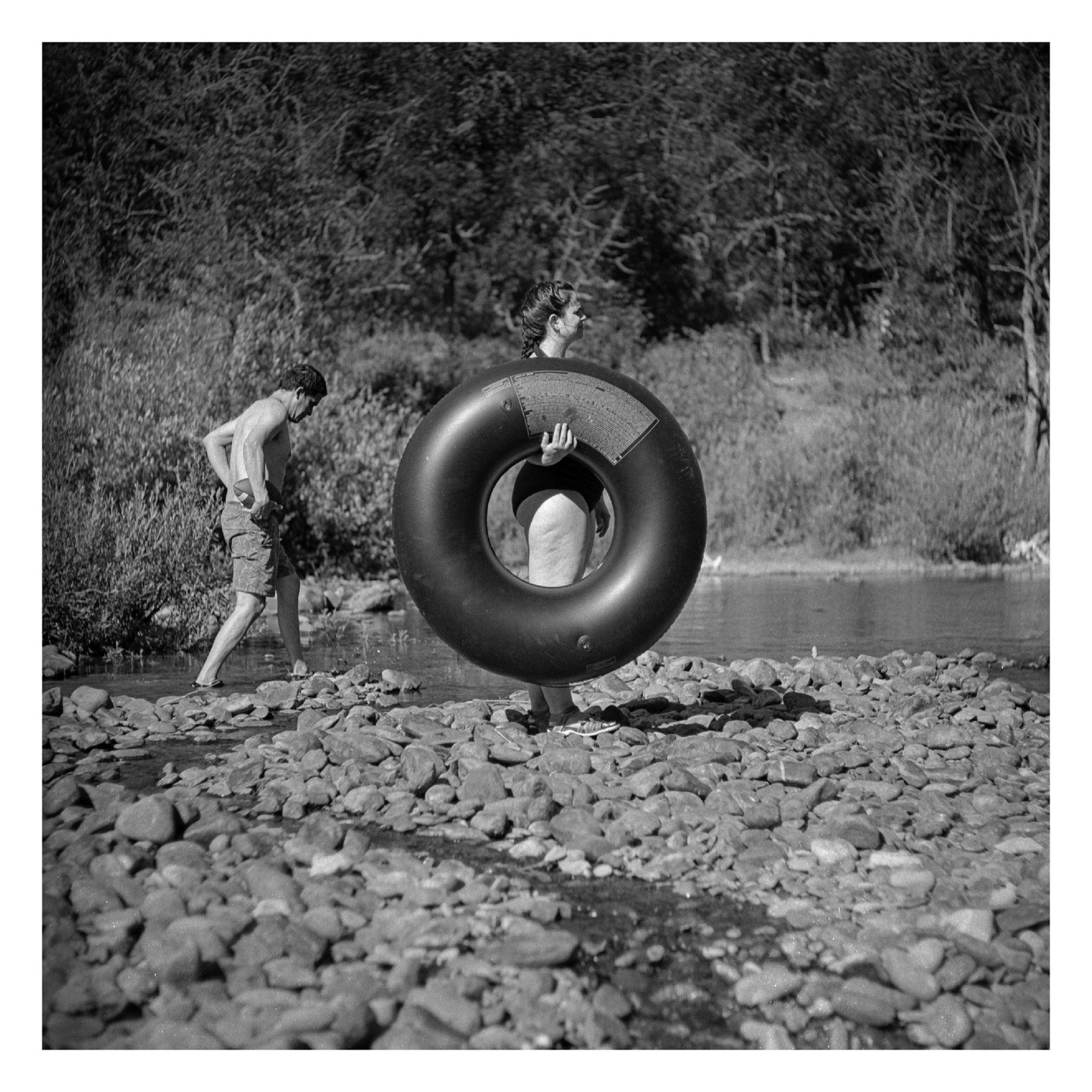 A man and a woman with an inner tube stand on a rocky riverbank.