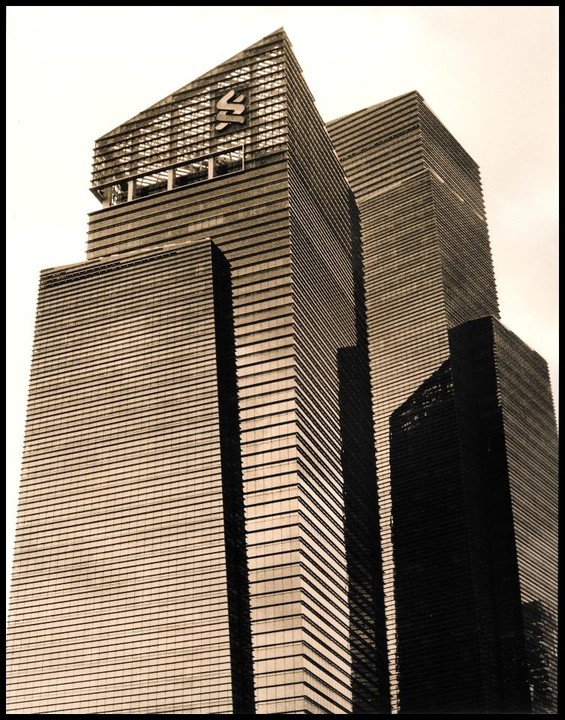 Three skyscrapers with horizontal lines and a logo on the tallest building are viewed from a low angle.