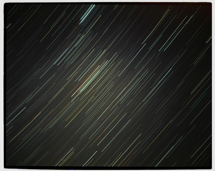 A long exposure photograph captures the movement of stars across a dark night sky, creating streaks of light.