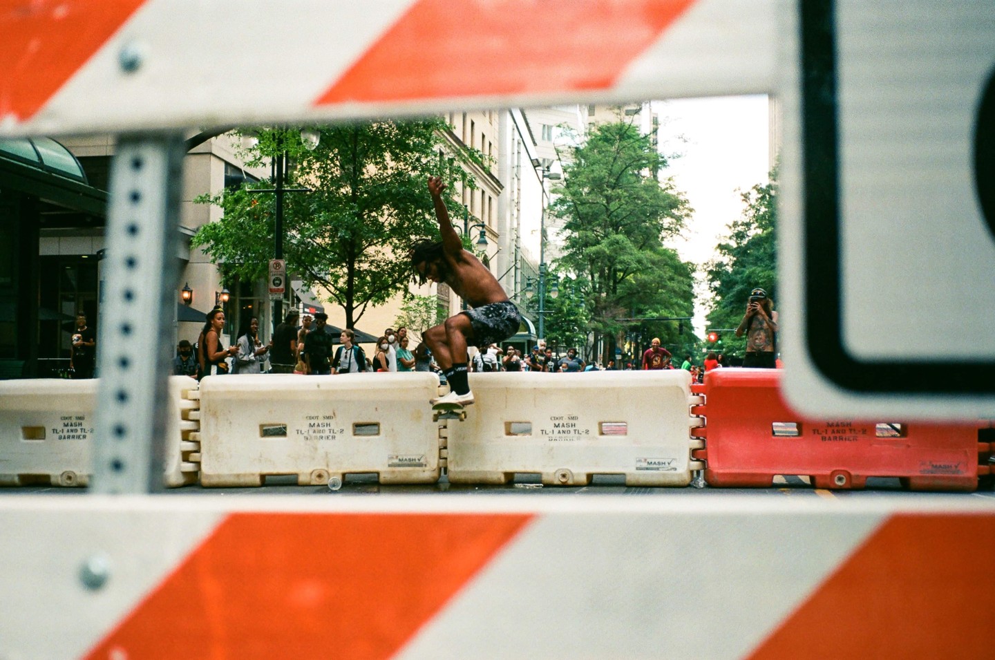 A skateboarder performs a trick on a street barrier while people watch in the background.