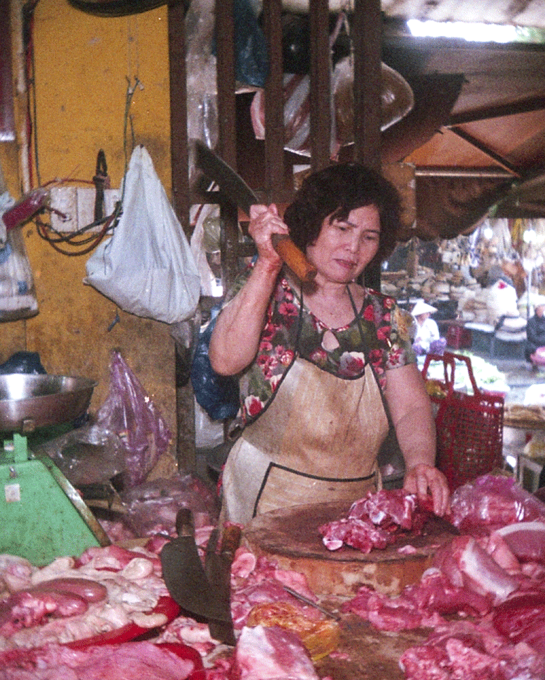 A woman in an apron holds a cleaver over a pile of meat in a market.