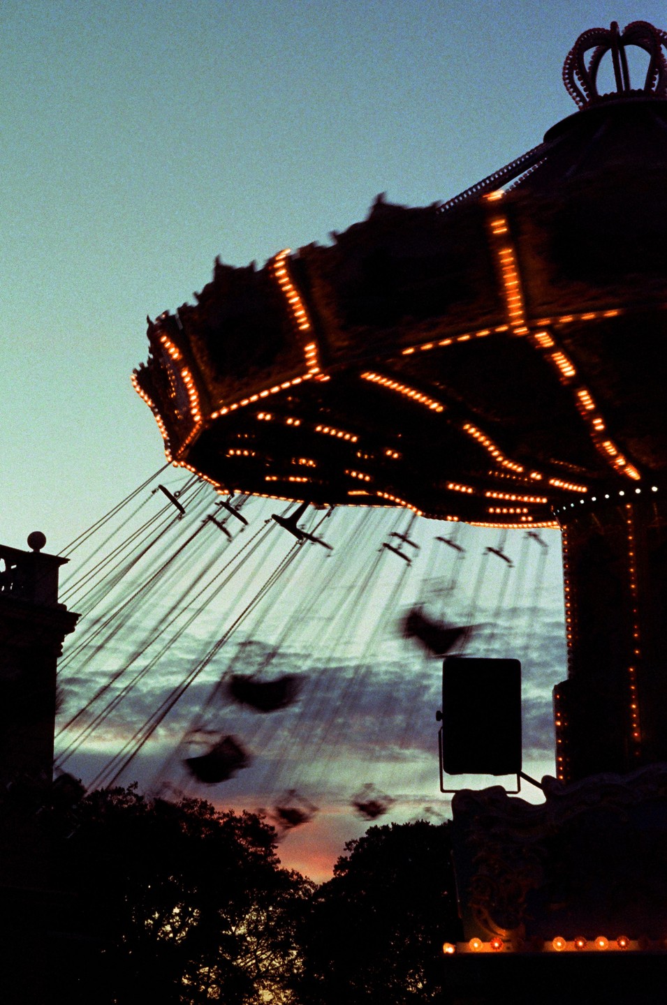 A swing ride with illuminated lights is silhouetted against a twilight sky with a colorful sunset.