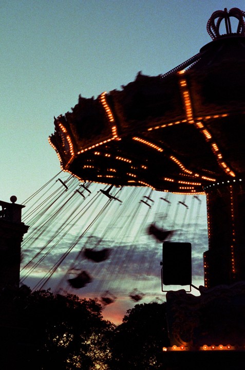 A swing ride with illuminated lights is silhouetted against a twilight sky with a colorful sunset.