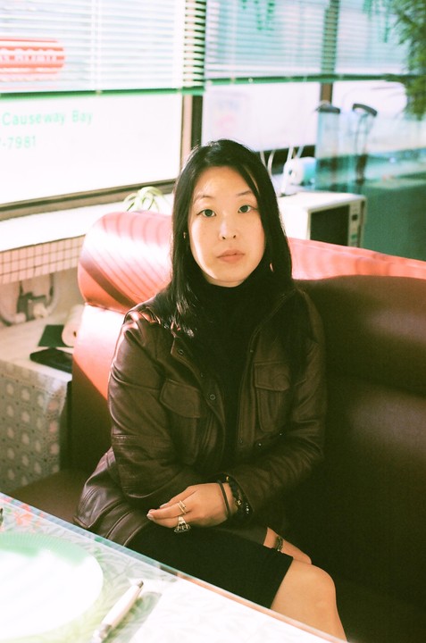 A woman sits in a booth at a diner with sunlight streaming through the window.
