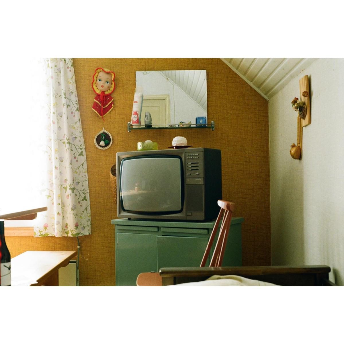 A vintage television sits on a green cabinet next to a window with a floral curtain.