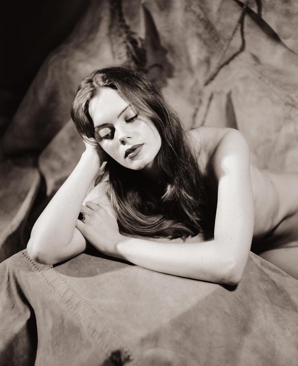 A woman with long hair and closed eyes rests her head on her arm.