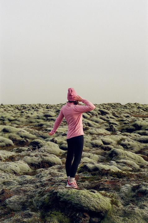 A woman in a pink hat and shirt stands on a mossy landscape under a pale sky.
