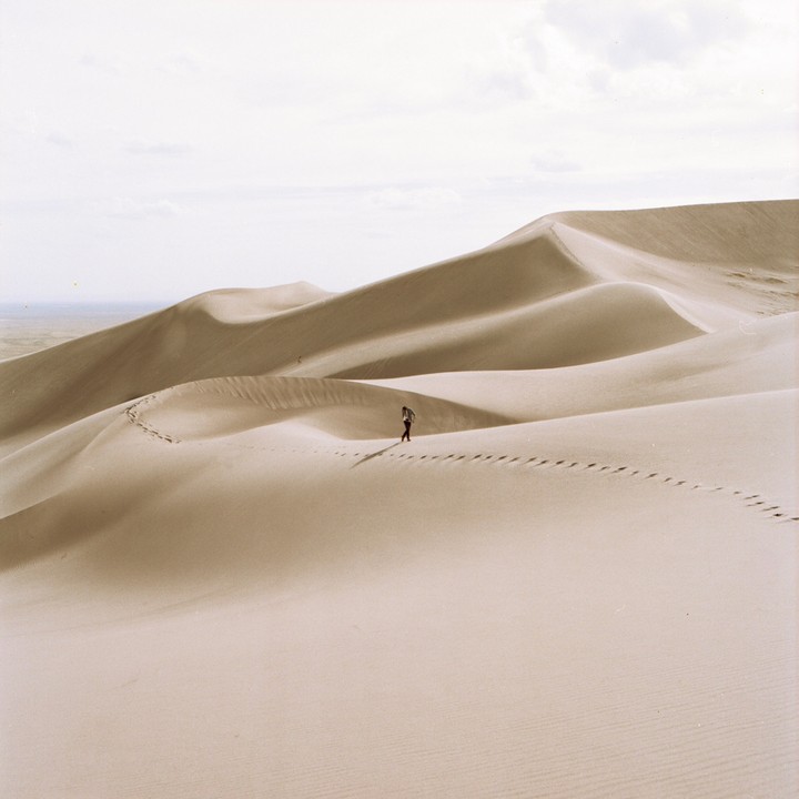 A person walks along a ridge of sand dunes, leaving footprints behind them.