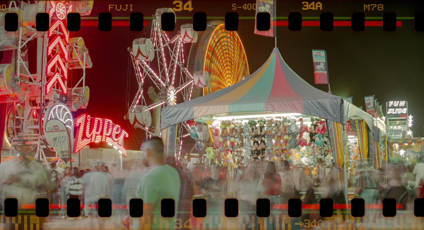 A long exposure captures the motion of people and rides at a night carnival.