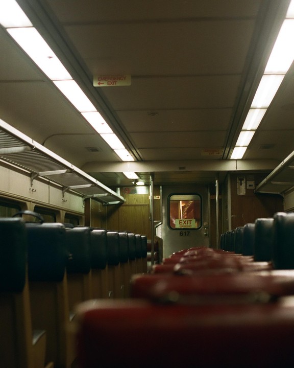 The interior of a train car is visible, with rows of seats and an exit sign on the door.