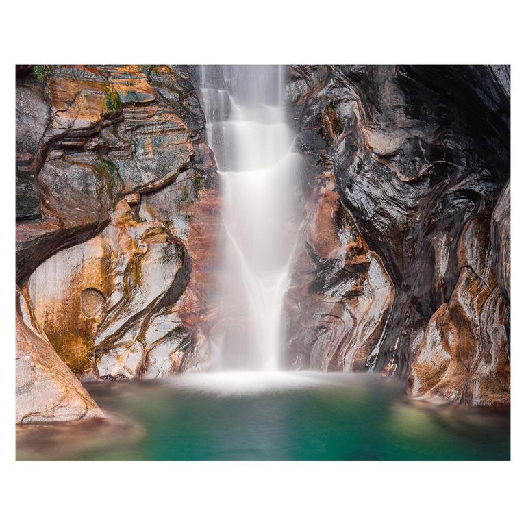 A waterfall cascades into a pool of turquoise water surrounded by colorful rock formations.