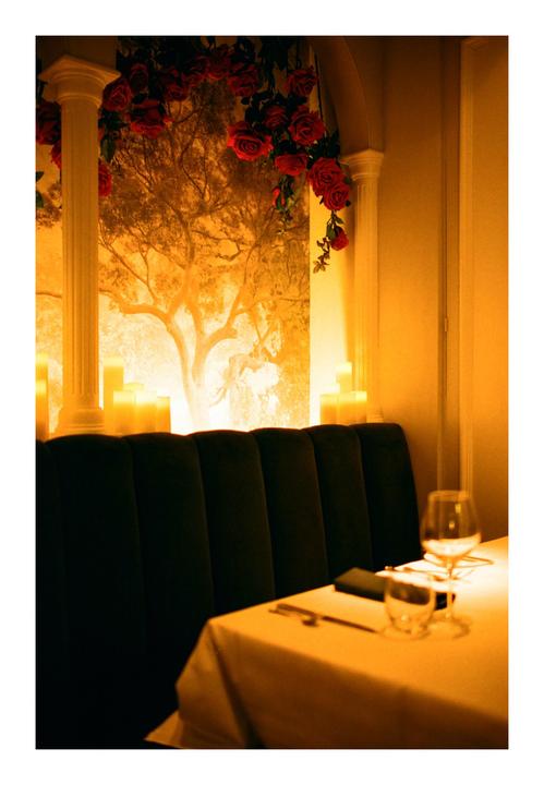 A restaurant booth with a table set for two is illuminated by candles and a mural of a tree.