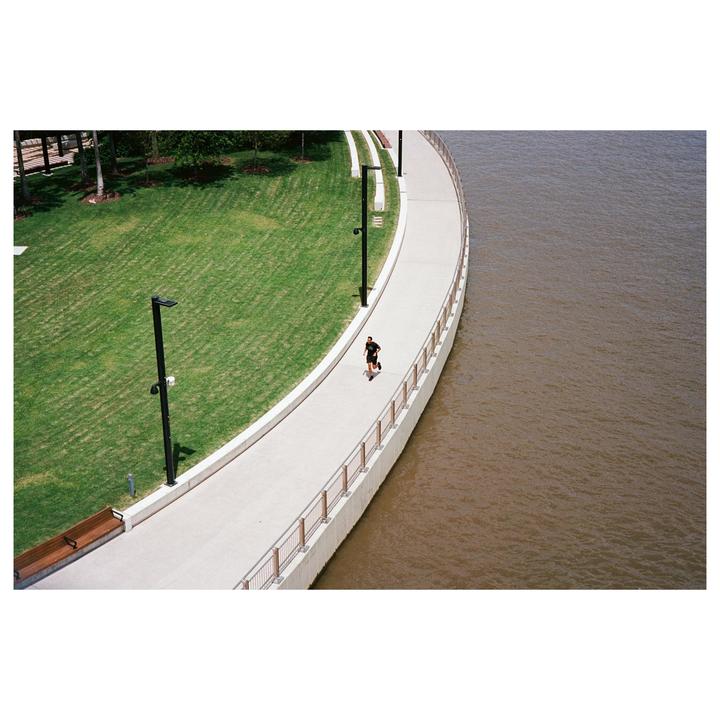 A man runs along a curved path next to a body of water and a grassy area.
