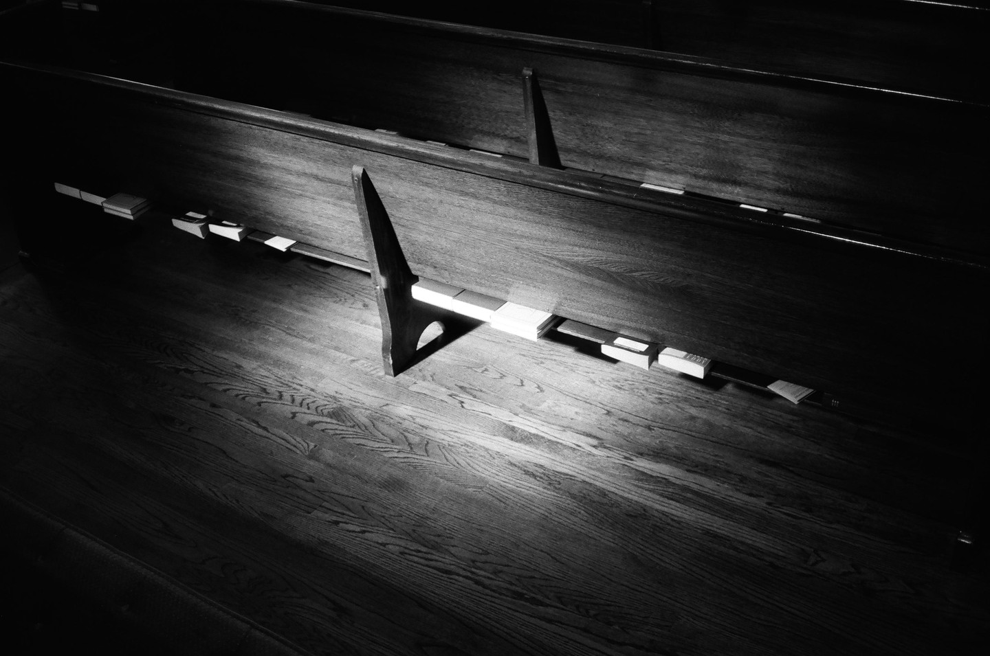 Sunlight illuminates hymnals and a wooden pew in a church.