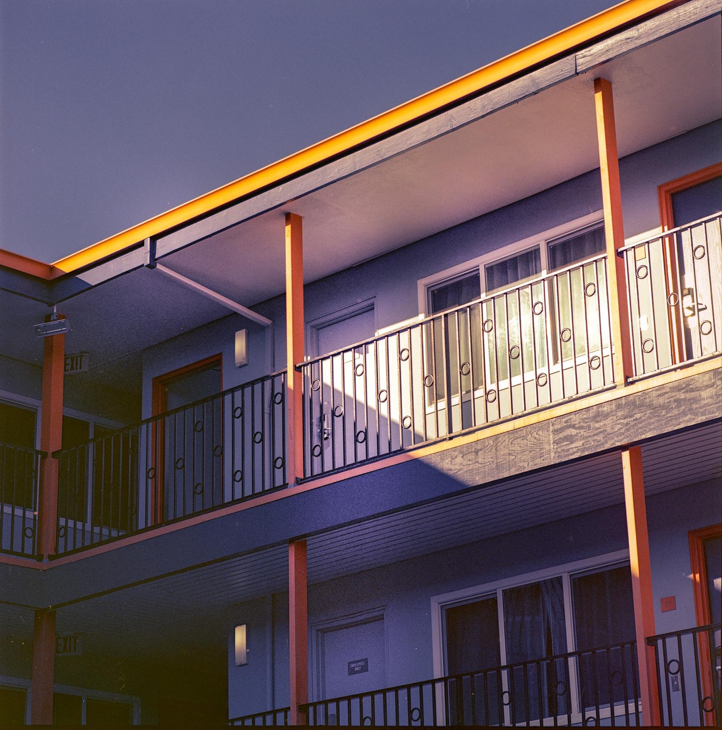 A motel building with orange pillars and railings is partially illuminated by sunlight.