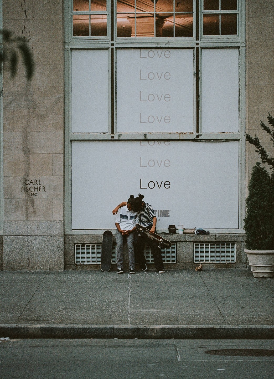 Two young men with skateboards sit on a ledge in front of a building with "Love" written on its windows.
