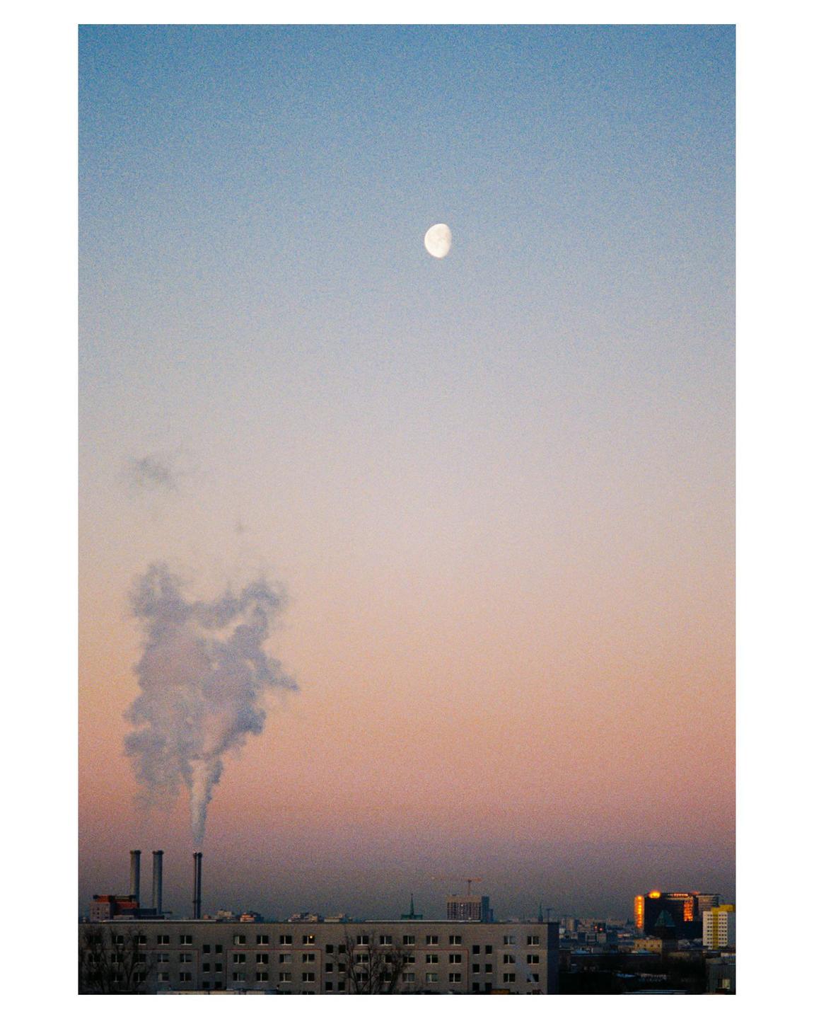 A full moon hangs in a gradient sky above a city skyline with smoke rising from industrial chimneys.