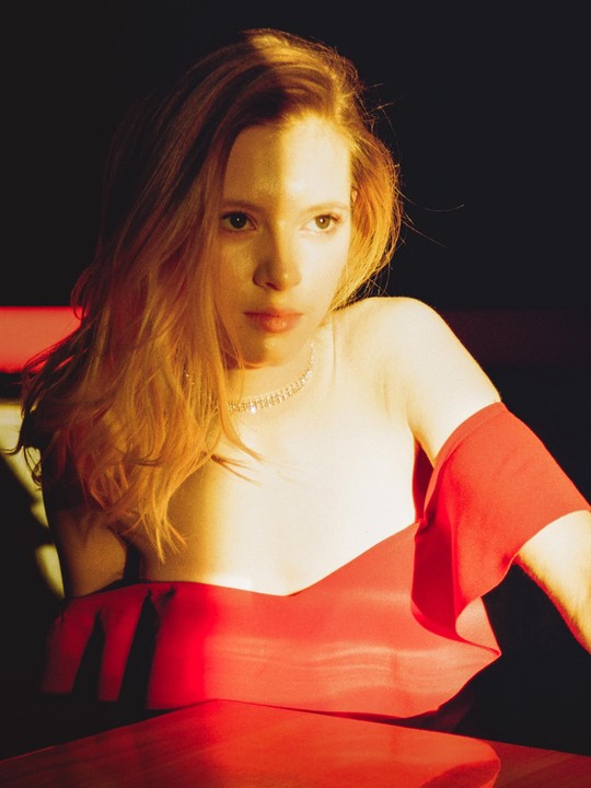 A woman in a red dress is illuminated by a strong light source that casts a shadow across her face.