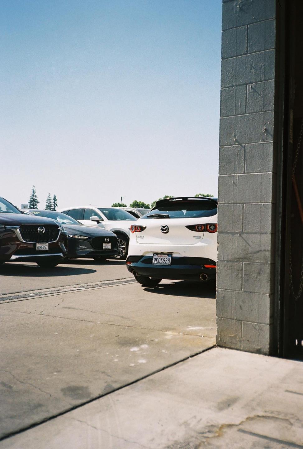 Several cars are parked on a paved lot next to a building with a large open doorway.