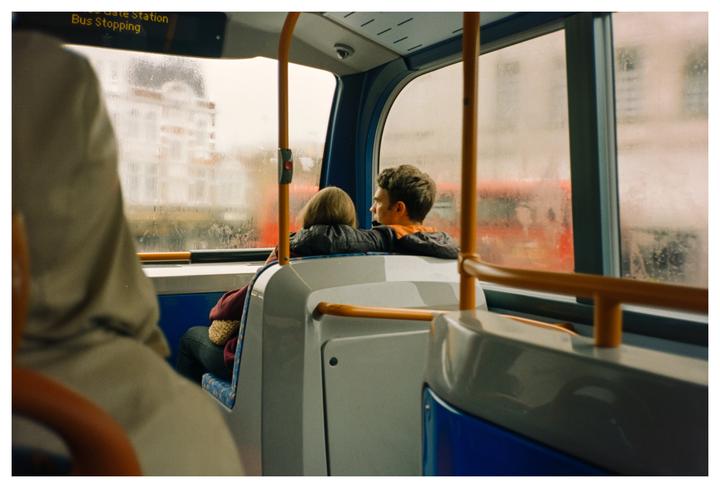 A couple sits on a bus looking out a window on a rainy day.