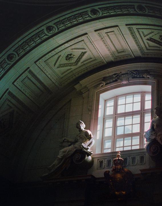 A statue of a woman is illuminated by light from a window in a grand, ornate building.