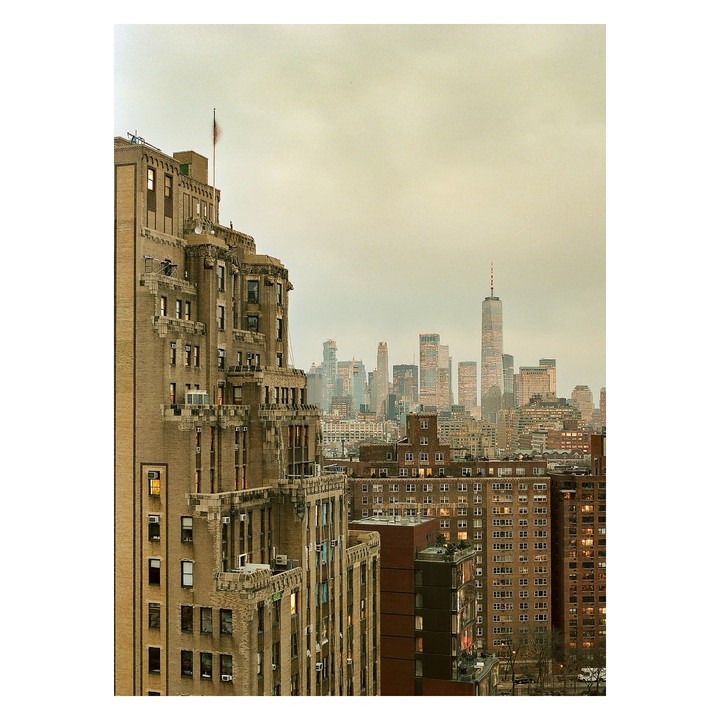 A tall building with a flag on top stands in the foreground, overlooking a city skyline with many skyscrapers.