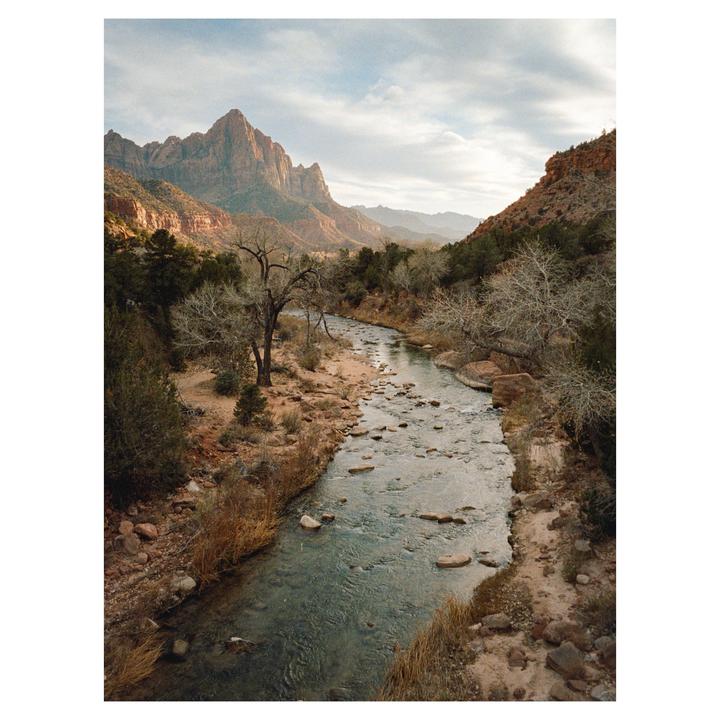 A river flows through a valley with mountains in the background under a cloudy sky.
