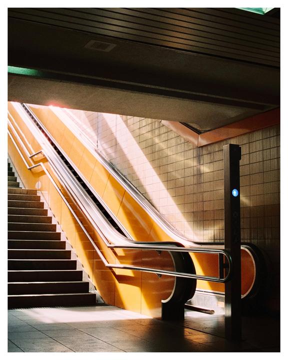 Sunlight illuminates an escalator and a staircase in a subway station.