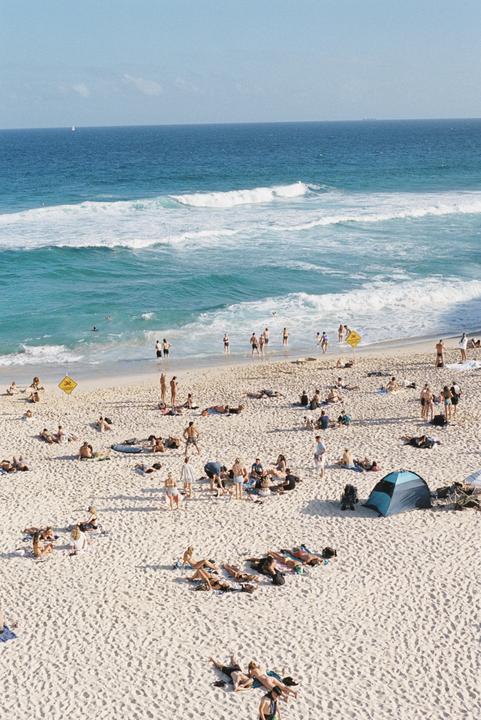 A large crowd of people are relaxing on a sandy beach next to the ocean.