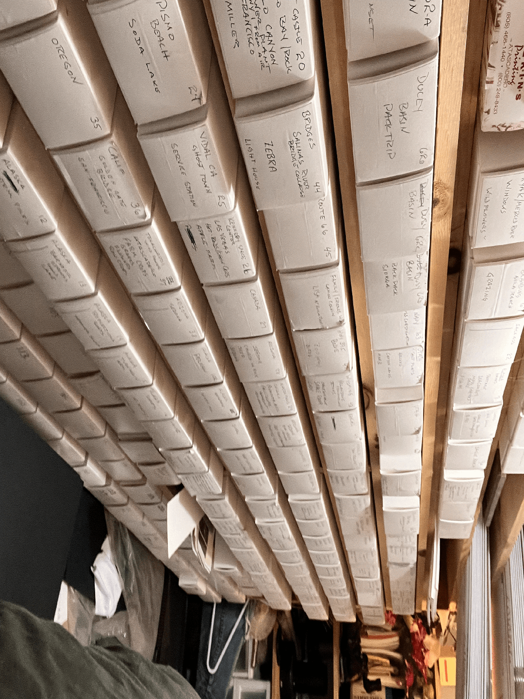 Rows of white boxes with handwritten labels are stacked on wooden shelves.